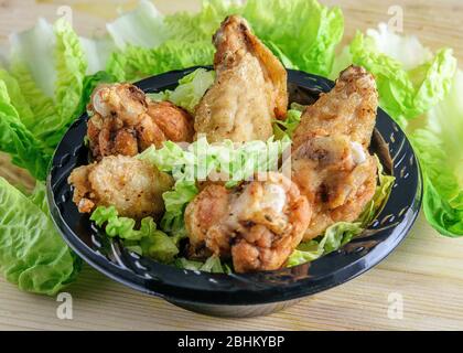Fried crispy chicken wings in the plate, green lettuce on the wooden table. Fast food concept. Stock Photo