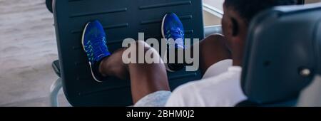 Back view of African American man doing exercise on leg press during fitness training in modern gym. Stock Photo