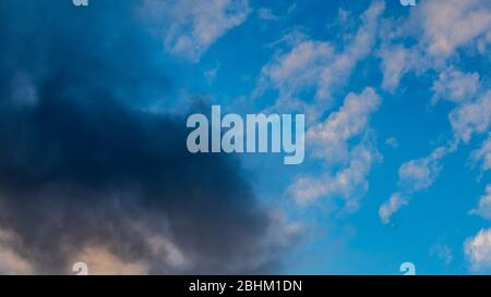 A storm cloud encroaches on blue sky as turbulent weather approaches. Stock Photo