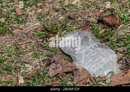 A plastic water bottle has been flattened and sits on the grass outside. Stock Photo
