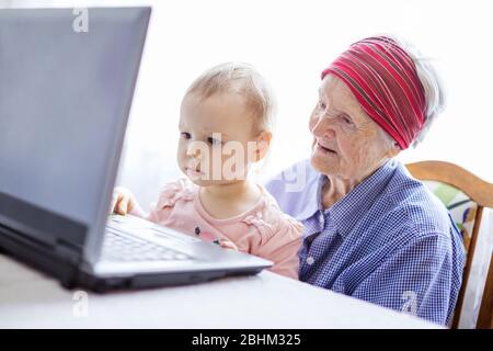 Senior woman and her great granddaughter looking at screen of laptop computer during video call from home Stock Photo