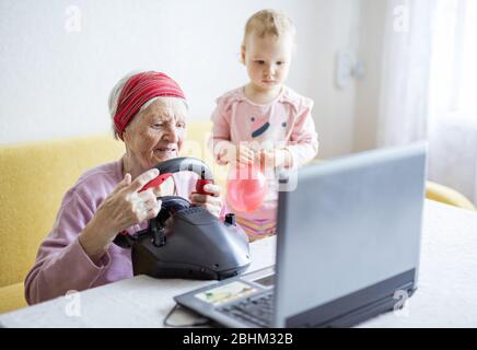 Senior woman and her great granddaughter enjoying car racing video game on laptop at home Stock Photo