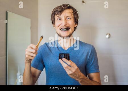 Young man brush teeth using Activated charcoal powder for brushing and whitening teeth. Bamboo eco brush Stock Photo