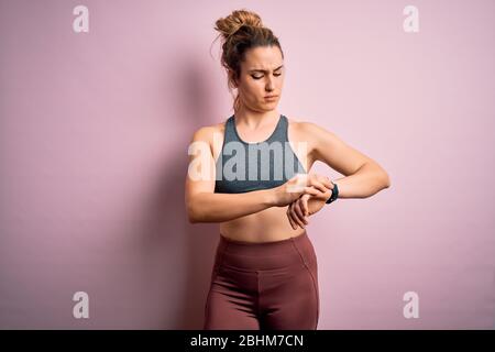 Young beautiful blonde sportswoman doing sport wearing sportswear over pink background Checking the time on wrist watch, relaxed and confident Stock Photo