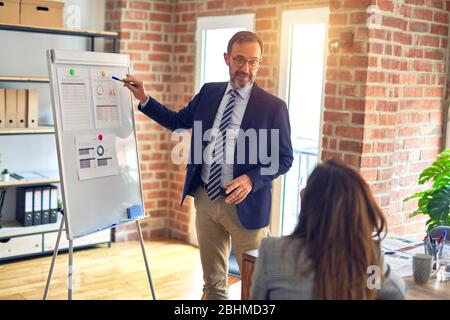 Two middle age business workers smiling happy and confidentt working together with smile on face. Man standing doing work presentation using board and Stock Photo
