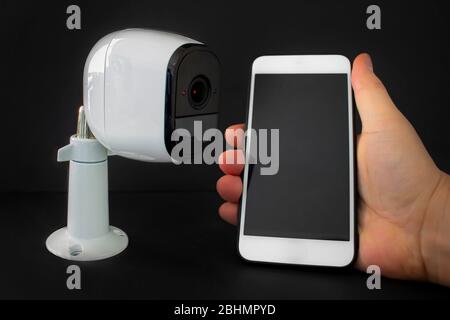 A smart security camera with a smart phone hold by a person Stock Photo