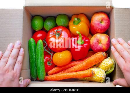 A person opening a deliver cardboard box with produce, fruits and vegetables inside on a white background Stock Photo