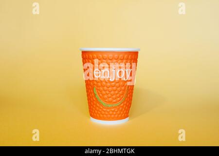 Orange paper environmental mug with the words Enjoy and smile on a bright yellow background Stock Photo