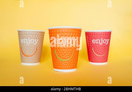 Three paper environmental mug in different colors with the inscription Enjoy and smile on a bright yellow background Stock Photo