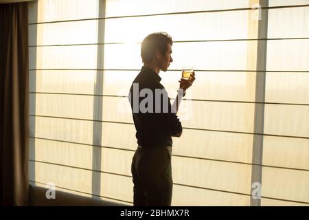 Young Chinese businessman drinking alcohol in front of window Stock Photo