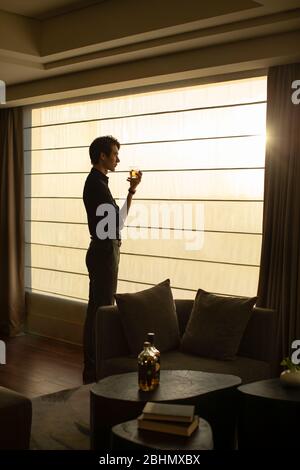 Young Chinese businessman drinking alcohol in front of window Stock Photo