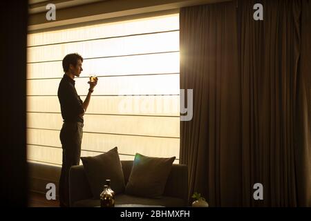 Young Chinese businessman drinking alcohol in front of window Stock Photo