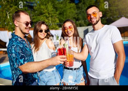 Group of friends having fun at poolside summer party clinking glasses with summer cocktails on sunny day near swimming pool. People toast drinking Stock Photo