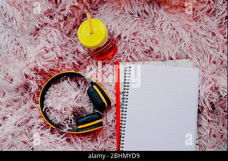 open empty large notebook on a spiral, yellow wireless headphones and a yellow mug with a tube on a pink fluffy blanket. a cozy place to practice duri Stock Photo