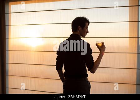 Young Chinese businessman drinking alcohol in front of window Stock Photo