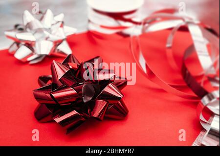 large red foil bow for packaging and decoration on a red and silver background and packing ribbons on the background. Stock Photo