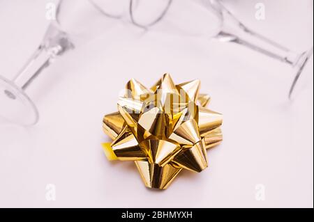 gold foil bow on delicate beige paper and two clean empty glasses on the background Stock Photo