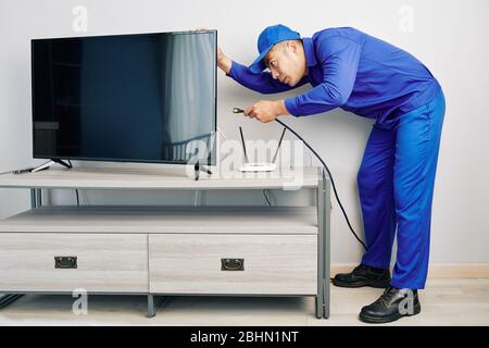 Serious young Vietnamese repairman installing tv set in apartment of customer Stock Photo