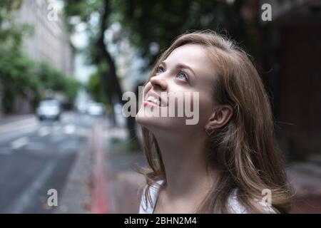 Portrait of a beautiful girl with mysterious, flirty, coquettish look on her face with city street on the background Stock Photo