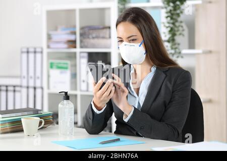 Executive woman with protective mask using smart phone sitting on a desk at the office Stock Photo