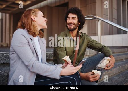 Happy laughing couple enjoying sandwich during lunch break Stock Photo