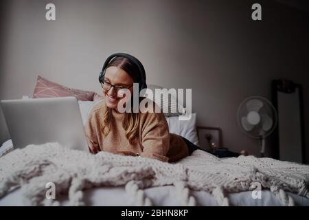 Young woman with glasses wearing headphones listening to music and taking online classes - young student on a online video call  Stock Photo