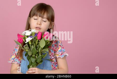 Cute smiling adorable child girl holding bouquet of spring flowers isolated on pink background Stock Photo