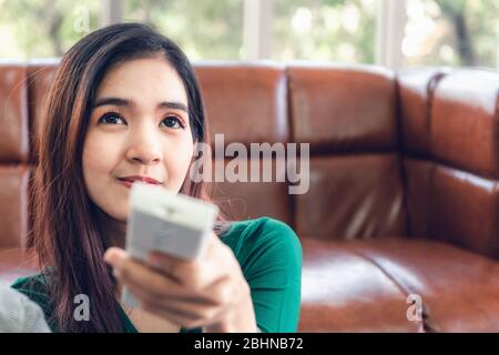 Close-Up of Asian Woman is Turn-On/OFF Air Conditioner Split Type by Remote Controller in Living Room. Electronic Air Conditioning for Comfortable Tem Stock Photo