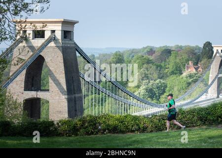 Clifton, Bristol, UK. 25th April 2020. A lone runners passes in front of the Clifton Suspension Bridge on what promises to be one of the warmest days Stock Photo