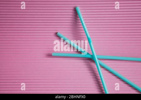 Blue drinking straws on a pink background, without a plastic Cup. Colorful summer background with Sunny shadows.Top view. Stock Photo