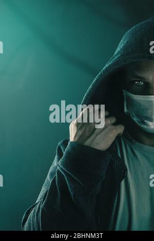 Dark photo of Young handsome man wearing medical protactive face mask and hood in the night Stock Photo