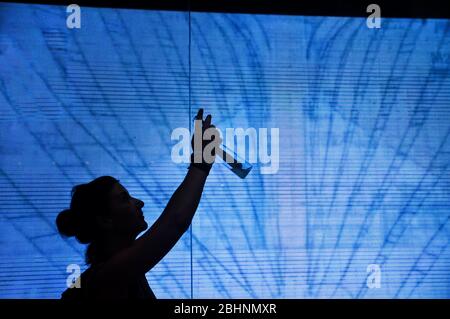 A silhouette of a woman standing in front of a wall of screens take a picture with smartphone. Stock Photo
