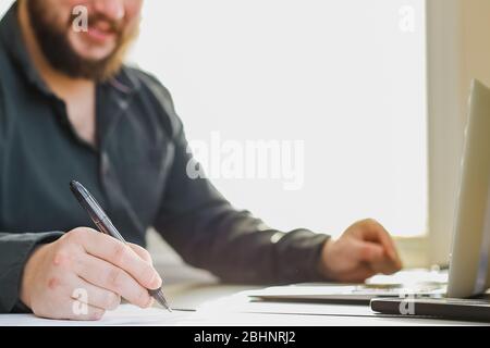 Focus on pen, male author writing new book and using laptop. Stock Photo