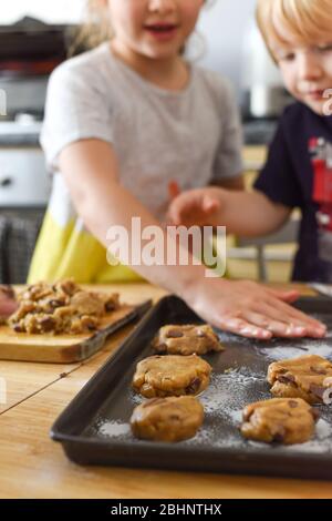 Kids making cookies in kitchen placing dough on tray for cooking at home Stock Photo