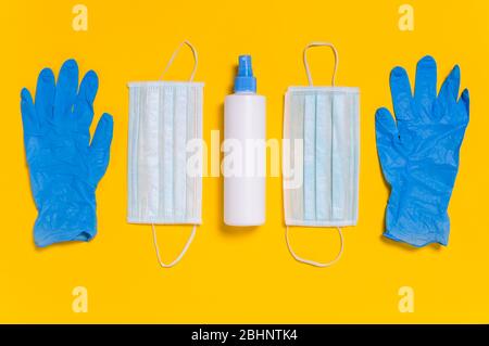 Coronavirus protection. Medical surgical masks, disinfectant or hand sanitizer and blue disposable gloves on yellow background. Hygiene measures to pr Stock Photo