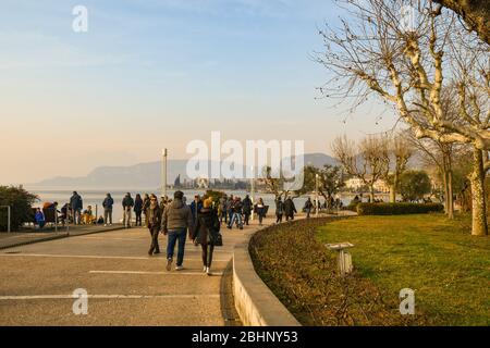 People and tourists walking on the lakeside promenade of the old town of Bardolino on the shore of Lake Garda in winter at sunset, Verona, Italy Stock Photo