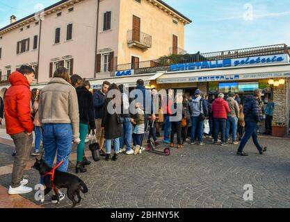 A lot of people standing in line waiting to buy ice cream outside an ice cream shop in the old town of Bardolino, Lake Garda, Verona, Veneto, Italy Stock Photo