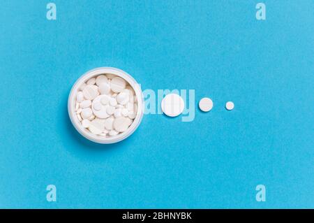 Medicine bottle with white pills inside and dosis of different size pills outside on blue background. Madication and prescription pills flat lay backg Stock Photo