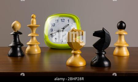 Two knights facing each other on a wooden table, with an alarm clock and other chess pieces in the background Stock Photo