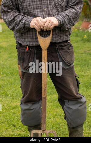 A man's hands resting on a garden fork's grip Stock Photo