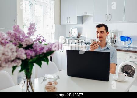 Young businessman working from home during coronavirus lockdown using laptop and smartphone having coffee. Stock Photo