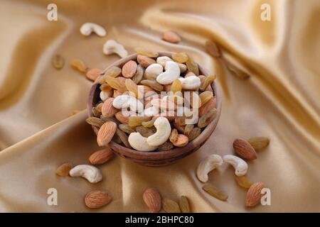 Delicious and healthy mixed dried fruit, nuts and seeds in a wooden bowl on golden silky background. Stock Photo