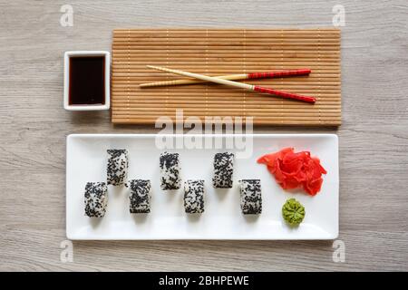 Originally laid out sushi roll on a white plate. With chopsticks, ginger, wasabi and soy sauce on a white small bowl Stock Photo