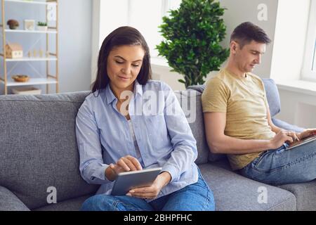 Middle-aged couple people use a laptop tablet gadget while sitting on the sofa in the room. Stock Photo