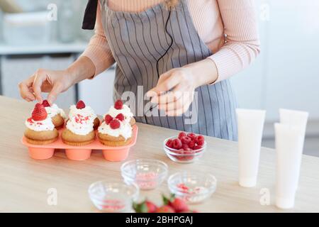 Horizontal high angle shot of unrecognizable young woman decorating homemade cupcakes with fresh berries Stock Photo