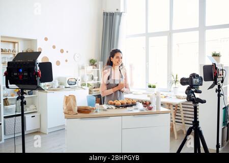Professional baker standing alone in kitchen recording cupcakes cooking process video on camera for her vlog channel Stock Photo