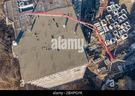 Pouring cement on the floors of residential multi-story building under construction using a concrete pump truck with high boom to supply the mixture t Stock Photo