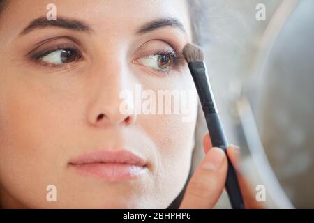 Horizontal close-up portrait of young adult woman applying eyeshadow on her eyelid using brush Stock Photo