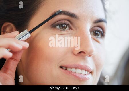 Close-up shot of beautiful young adult Caucasian woman fixing her eyebrows with gel Stock Photo