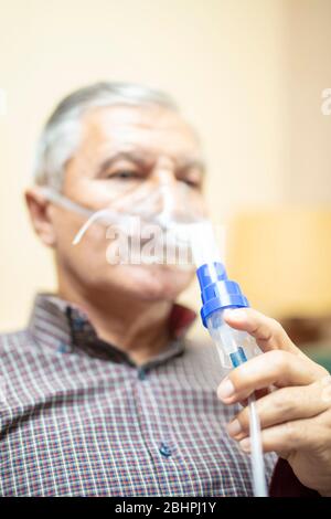 Senior man using medical equipment for inhalation with respiratory mask, nebulizer in the room Stock Photo